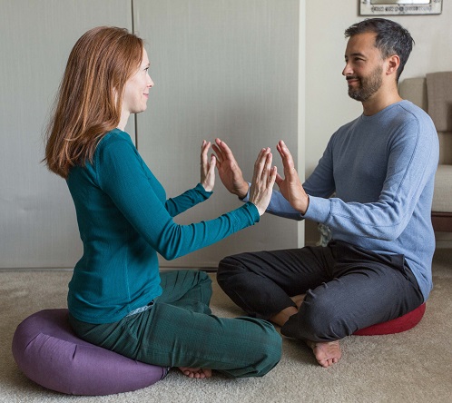 Caucasian female and male sitting with legs crossed facing each other with palms close to touch and smiling faces