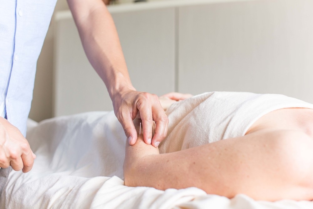 Acupuncture treatment with patient on bed and therapist applying needle point to patient's left forearm