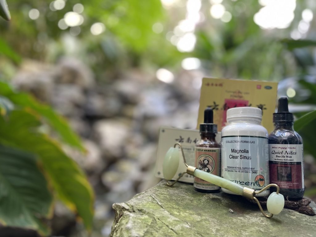 Featured health products from Healthy Qi with tincture and capsule supplements showing outdoors on rocks with greenery and water flowing in the background